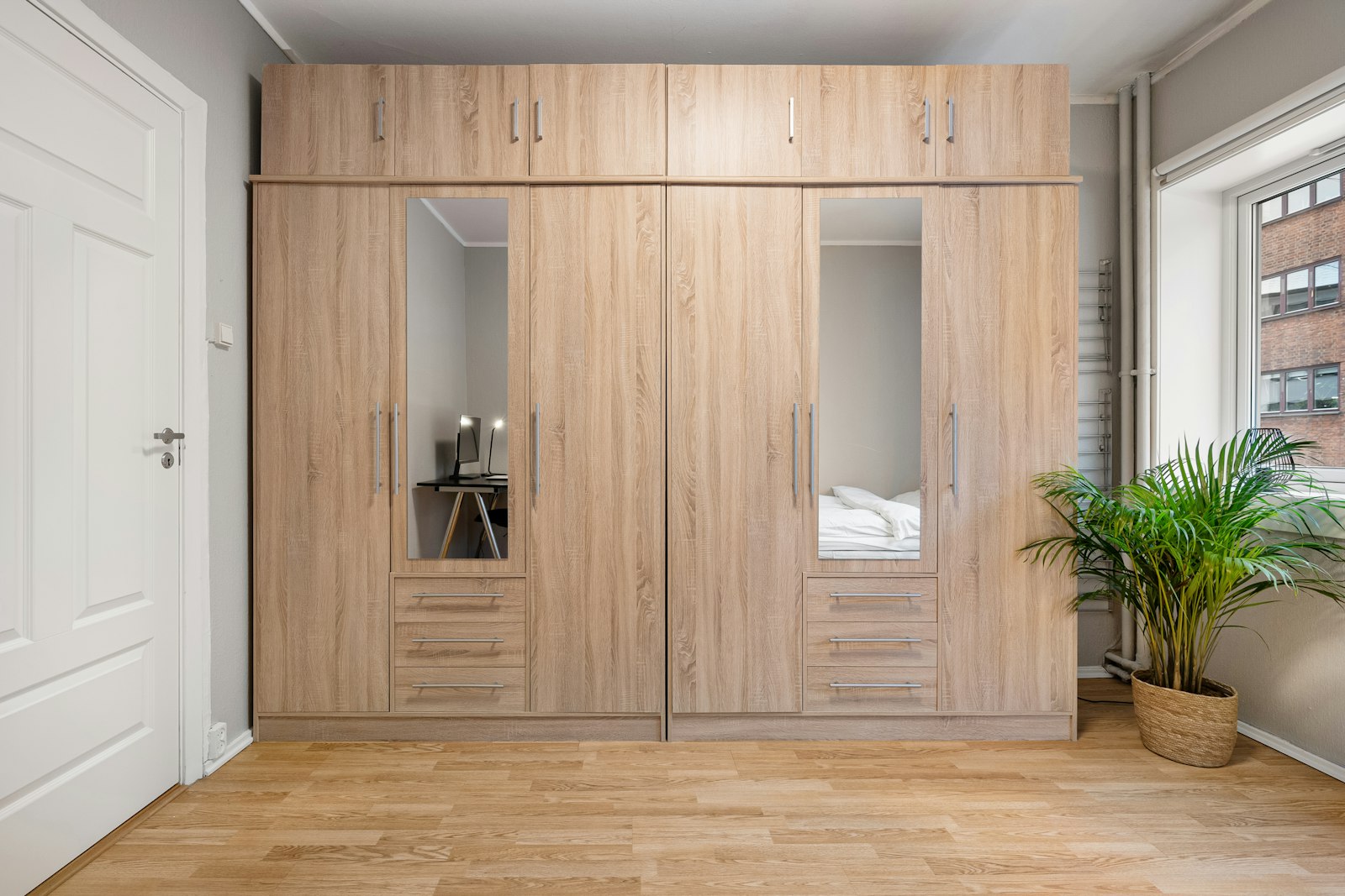 A built in light wood wardrobe with mirrored doors in a bedroom